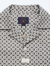 Close-up of a Blue de Gênes Colonnello Delo shirt with a multi-pattern design in black and white. The open collar reveals a black necklace with a small pendant, while two labels are visible near the neckline.