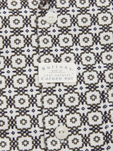 A close-up of the Colonnello Delo shirt by Blue de Gênes showcases a jacquard pattern in black and white, reminiscent of their geometric elegance. The cotton fabric features white circular buttons with a label stating theyre made from real natural Corozo nut.