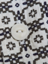Close-up of a white button sewn with white thread onto the Colonnello Delo shirt by Blue de Gênes, showcasing a jacquard pattern with black and grey squares and crosses on crisp white cotton.