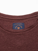 Close-up of the Totti T-Shirt - Prune by Blue de Gênes showcasing its neckline with a blue tag, featuring Italian text and a logo on a white background. The focus is on the shirts natural texture, crafted from 100% Linen Jersey.