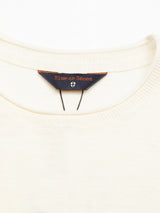 The close-up of a white Monte Knit - Whitecap sweater by Blue de Gênes shows the dark blue label adorned with a small crest symbol on the crewneck. Made from a soft cotton/linen blend, this fine knit piece offers both style and comfort.