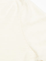 A close-up of the Monte Knit - Whitecap by Blue de Gênes reveals a roll-rib hem on the sleeve and part of the shoulder seam in a plain beige or off-white. The fabric, a soft cotton/linen blend, exhibits a slightly textured appearance.