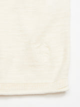 Zoom in on the Monte Knit - Whitecap by Blue de Gênes, showcasing a white fabric with a subtle embroidered shield pattern near the edge. The texture emphasizes a simple knit made from a cotton/linen blend, finished cleanly.