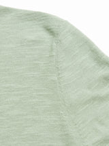 Close-up of the Monte Knit - Green Bay by Blue de Gênes, featuring a light green fabric crewneck with visible stitching and textured cotton/linen blend. The image highlights the weave, seam detail, and the fabrics soft, muted color.