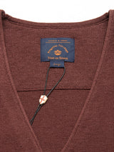 Close-up of the prune Zorba Knit Waistcoats collar, featuring a blue label with brown text and a small shield charm on a string. The label reads Blue de Gênes, indicating the brand and size as large, crafted from luxurious merino wool.