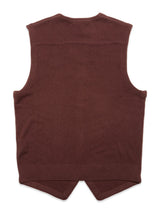 The image features the back view of the Zorba Knit Waistcoat - Prune by Blue de Gênes, a brown sleeveless merino wool vest with a ribbed hemline and two pointed edges at the bottom, appearing smooth and lightweight.