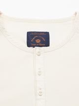 Close-up of the Nipote AW S/S Grandad T-Shirt in cream, featuring a classic design with a short button placket and white buttons. Made from cotton interlock jersey, it has a navy label with orange text inside the collar stating Blue de Gênes.
