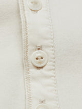 Close-up of the Blue de Gênes Nipote AW S/S Grandad T-Shirt in Whitecap, made from cotton interlock jersey with a row of light-colored buttons. Visible stitching alongside the buttons showcases its detailed texture and classic design.