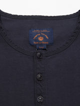 Close-up of a dark henley shirt with a collarless design and four black buttons. The tag reads Nipote AW S/S Grandad, Blue de Gênes, Large, on a dark blue background with orange text. This Grandad T-Shirt style offers comfort and style.