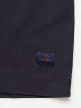 A close-up of the Nipote AW S/S Grandad - Dark Navy by Blue de Gênes showcases a dark cotton interlock jersey fabric with a stitched navy patch, embroidered orange logo and text, and visible hem of its collarless design.