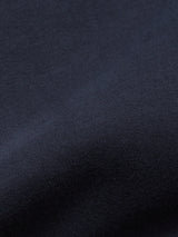 A close-up of Blue de Gênes Nipote AW S/S Grandad in Dark Navy reveals a smooth cotton interlock jersey with a soft texture. The evenly woven material mimics its collarless design, with subtle shadows and highlights playing gently across the fabric surface.