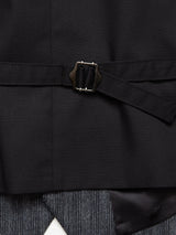 The Canna Dori Gilet by Blue de Gênes features a black suit jacket with a belted metal buckle. Beneath, gray striped trousers in an Italian cotton-wool blend, crafted with Portuguese tailoring, complete the layered look.