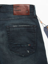 Close-up of Blue de Gênes Vinci Haworth Jeans in denim blue, showcasing the back pocket. Above, a leather patch displays the brand name. A fabric tag adorns the pocket edge, and a paper tag is pinned near the waistband. Made from Comfort Stretch Denim with a slightly distressed finish for style and ease.