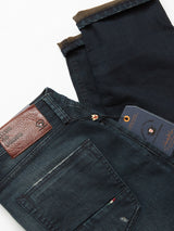 A close-up of Vinci Haworth Jeans - Denim Blue by Blue de Gênes shows dark blue denim with a brown leather waistband label, visible stitching, and a tricolor pocket detail. Made from Comfort Stretch Denim, these jeans promise ease of movement. A folded pair with brand tags lies beneath.