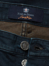 Close-up of Vinci Haworth Jeans in dark denim blue by Blue de Gênes, showcasing a black button with the brands name embossed. These Comfort Stretch Denim jeans offer flexibility, and the inside label displays the brand name in white and orange alongside a small logo.