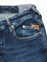 The Repi Scan Used Jeans by Blue de Gênes are mid blue denim comfort stretch jeans with detailed stitching, regular slim-fit, a front pocket, small coin pocket with metal rivets, and a leather patch above the coin pocket. A paper tag is visible from the waistband.