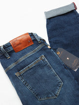 These Repi Scan Used Jeans from Blue de Gênes are mid blue denim with a brown leather brand patch on the waistband. They feature one cuffed leg to showcase the selvedge edge with red stitching and have a black tag. Made from comfort stretch denim, offering classic style and ease.