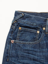 Close-up of Giacomo 77 Dark Used Jeans in mid-blue denim by Blue de Gênes, highlighting the pocket, belt loops, and stitching details. A small pin with a red shield and white cross is attached near the pocket.
