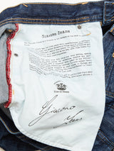 A close-up of the Giacomo 77 Dark Used Jeans by Blue de Gênes showcases a label emphasizing their robust construction with mid blue, rigid denim, inspired by Genoas dock workers and sailors. The jeans offer a relaxed loose fit that blends comfort with tradition.