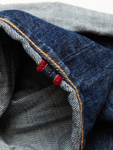 Close-up of Giacomo 77 Dark Used Jeans by Blue de Gênes, featuring rigid mid-blue denim with a selvage edge, dark blue hue, striking orange seam, red stitching, and a lighter blue inner side for distinctive craftsmanship.