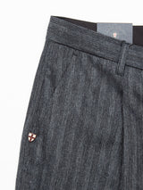 Close-up of Panco Dori Chino by Blue de Gênes in a relaxed fit, featuring irregular pinstripes on Italian cotton-wool blend, with a small round pin (red and white cross) on the waistband and partially visible dark tag at the top.