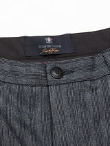 Close-up of the Panco Dori Chino waistband by Blue de Gênes in an Italian cotton-wool blend. Features a button, buttonhole, and a dark label with text and a flag emblem. The fabric has an irregular pinstripe pattern for style.