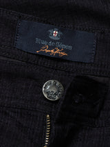 A close-up of Menzo Alvaro Chino - Navy shows dark denim with comfort stretch, featuring a metallic button engraved with Blue de Gênes, a partially open zipper, and a fabric label with the brand name and red and white emblem. The design offers style with tapered legs for modern elegance.