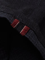 Close-up of a dark denim edge with visible red stitching, revealing a rugged, worn texture resembling the Menzo Alvaro Chino - Navy by Blue de Gênes, highlighting contrast between the dark material and bright red threads.