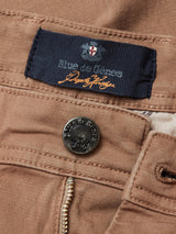 Close-up of brown Menzo Dobby Chino - Brownie pants with a Blue de Gênes label and a metal button engraved with the brand name. Their comfort stretch fabric and visible zipper offer style and ease of movement.