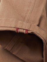 Close-up of a brown, rolled fabric with visible stitching and a hint of red thread reflects the vintage-inspired Menzo Dobby Chino - Brownie from Blue de Gênes, highlighting seam texture and offering comfortable stretch for daily wear.