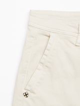 Close-up of Blue de Gênes Menzo Dobby Chino - Stone pants highlighting a pocket with a small gold and black diamond-shaped emblem near the seam. The soft, textured fabric provides comfort stretch for movement, while the waistband features belt loops and a button fastening for a vintage look.