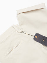 Stone Menzo Dobby Chino trousers from Blue de Gênes are folded neatly, showcasing a pocket and belt loop with an attached branded dark tag. Crafted from comfort stretch fabric, the vintage-style chinos are set on a plain white background.