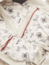 Close-up of the Menzo Dobby Chino - Stone by Blue de Gênes reveals beige fabric with printed text and anchor motifs. Red stitches and the pocket contribute to a vintage style, while the handwritten-style text highlights detailed craftsmanship.