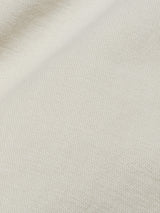 Close-up of a stone-colored Menzo Dobby Chino fabric by Blue de Gênes, showcasing a visible weave pattern with a diagonal fold. The texture features comfort stretch and appears soft, offering a gentle vintage look.