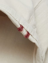 Close-up of a beige fabric from Blue de Gênes Menzo Dobby Chino - Stone, showcasing striking red stitching along a folded edge. The texture, vintage look, and contrast between the light fabric and dark stitches are clearly visible.