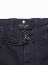 Close-up of dark navy Menzo Dobby Chino from Blue de Gênes, featuring a visible tag. The pants boast a vintage-inspired look, with a metal button at the waistband and comfort stretch for ease and style.