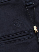 A close-up of the Menzo Dobby Chino - Dark Navy by Blue de Gênes reveals dark fabric with a small embroidered shield emblem for a vintage look, black cord with wooden toggle near a horizontal stitched pocket, and finely woven texture with comfort stretch.