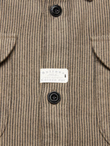Close-up of the Blue de Gênes Ginotto Oregon Shirt in Pebble Beige, showcasing a striped fabric with a label emphasizing real corozo nut buttons. The image features two black buttons next to a garment pocket, highlighting the classic fit style.