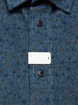 Close-up of a Blue de Gênes Enrico Cord Shirt - Blue Pattern with brown speckles and black corozo nut buttons down the front. The soft baby corduroy fabric features two visible black buttons and a collar.