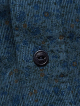 A close-up of the Blue de Gênes Enrico Cord Shirt - Blue Pattern features textured blue fabric with a subtle flower print in dark blue and brown tones, and a black button engraved with Cav Empt, reminiscent of ribbed baby corduroy.