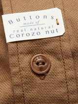 Close-up of brown cotton piqué fabric with a tag Buttons made of natural Corozo nut. A garment-dyed brown button features Blue de Gênes engraved on it. The ribbed texture resembles an Enrico Nidos Shirt - Fudge.