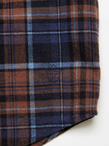 Close-up of the Zamboni Quadro Shirt - Navy Check by Blue de Gênes, displaying a plaid pattern in brown, black, blue, and light orange. Made from a winter cotton-linen blend with a small embroidered crest, this shirt has a soft texture and intricate yarn-dye check patterns for depth.