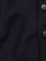 Close-up of the Peacoat in Dark Navy by Blue de Gênes, crafted from luxurious Melton wool. It features a left vertical slit pocket and branded buffalo horn buttons on the right, displaying a subtle fabric texture.