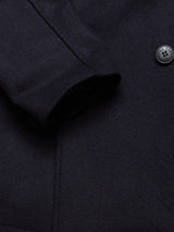 Close-up of a Dark Navy Peacoat by Blue de Gênes, featuring a single branded buffalo horn button. The textured Melton wool fabric and neatly sewn sleeve highlight fine stitching and craftsmanship.