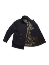 The Peacoat - Dark Navy by Blue de Gênes features branded buffalo horn buttons, a satin-like olive green lining with red piping, and is crafted from luxurious Melton wool. It showcases a timeless double-breasted design with two front pockets.