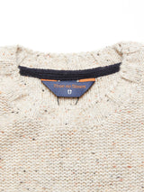 Close-up of Adamo Knit - Pebble Beige by Blue de Gênes, made from mélange yarn in light beige. Features a blue and brown neck label with the brand name and emblem. The cozy crewneck has a round neckline with dark inner trim.