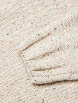 Close-up of the Adamo Knit - Pebble Beige sweater by Blue de Gênes, featuring a crewneck with a folded sleeve. The mélange yarn fabric has a textured look with multicolored specks that add subtle color variations to the neutral background.