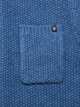 Close-up of the Aimone Knit Cardigan in Sugar Blue by Blue de GĂȘnes, featuring a lambswool honeycomb pattern with a central pocket and a logo patch above showing a shield with a cross and crown.