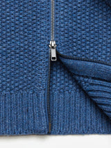 Close-up of the Aimone Knit Cardigan in Sugar Blue by Blue de GĂȘnes, showcasing its lambswool coarse pearl knit fabric with a textured pattern. A silver zipper is partially unzipped, and the ribbed hem is visible at the bottom.