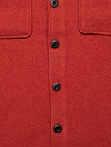 Detail of the Blue de GĂȘnes Pampa Overshirt in Ochre Red, highlighting its soft boiled wool fabric and black Corozo buttons. The garment features pocket flaps and exudes the casual charm typical of an overshirt.